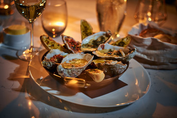 Rich and luxury dinner golden metallic bowl of prepared oysters and crispy bread loafs with sauce and vegetable spread served on a white stone table next to candle, a glass of white wine, jellyfish in