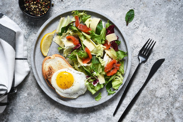 Fried eggs with toast, green salad with salmon on the kitchen table.