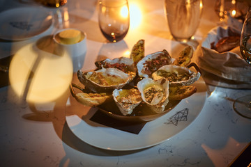 Rich and luxury dinner golden metallic bowl of prepared oysters and crispy bread loafs with sauce and vegetable spread served on a white stone table next to candle, a glass of white wine, jellyfish in
