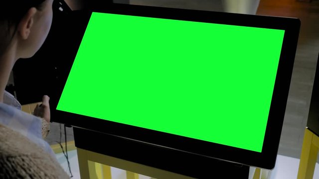 Green screen, mock up, future, copyspace, template, chroma key, technology concept. Woman looking at blank interactive touchscreen green display of electronic kiosk at futuristic exhibition or museum