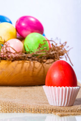 Red easter egg in a white stand on a napkin on a wooden plate with eggs.