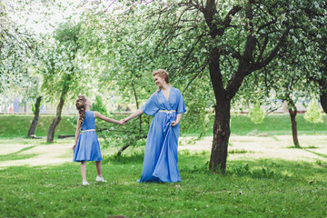 Naklejka na ściany i meble cheerful mother and daughter in dresses walk in the spring park