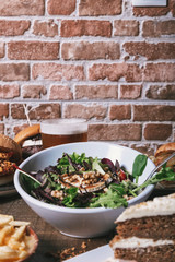 Salad with goat cheese, homemade hamburgers with french fries, drink and cake on the wooden table. Isolated vertical image.