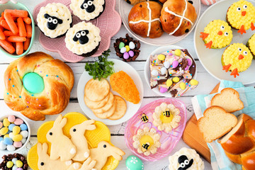 Easter table scene with a selection of breads, desserts and treats. Above view over a white wood background. Spring holiday food concept.