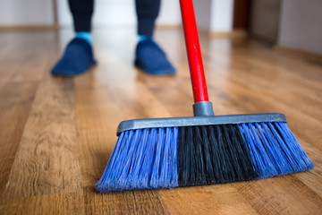 Wife in blue slippers using indoor blue broom for hardwood floor cleaning.