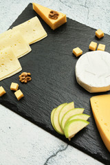 Pieces of cheese on a dark background. Cheeseboard. Sliced ​​apple and nuts on the board. Hard cheese, camembert, roquefort, emmental.