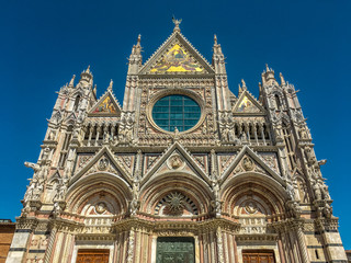 Fototapeta na wymiar Main Facade of Duomo di Siena—13th-century Romanesque-Gothic Cathedral with mosaics and marble stripes on facade.