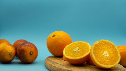 Oranges cut in half on a wooden board on a blue background with blood oranges on the right side of the image. Healthy food concept.