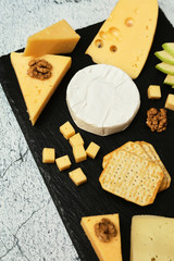 Pieces of cheese on a dark background. Cheeseboard. Sliced ​​apple and nuts on the board. Hard cheese, camembert, roquefort, emmental.