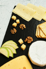 Pieces of cheese on a dark background. Cheeseboard. Sliced ​​apple and nuts on the board. Hard cheese, camembert, roquefort, emmental.