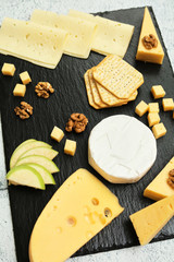 Pieces of cheese on a dark background. Cheeseboard. Sliced ​​apple and nuts on the board. Hard cheese, camembert, roquefort, emmental.
