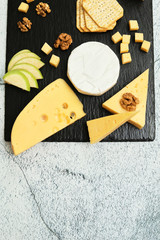 Pieces of cheese on a dark background. Cheeseboard. Sliced ​​apple and nuts on the board. Hard cheese, camembert, roquefort, emmental.