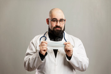 Male doctor in a white coat with a medical mask in his hands. Gray background.