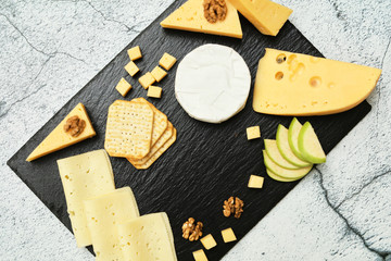 Pieces of cheese on a dark background. Cheeseboard. Sliced apple and nuts on the board. Hard cheese, camembert, roquefort, emmental.