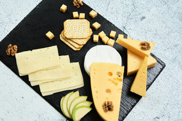 Pieces of cheese on a dark background. Cheeseboard. Sliced ​​apple and nuts on the board. Hard cheese, camembert, roquefort, emmental.