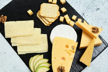 Pieces of cheese on a dark background. Cheeseboard. Sliced ​​apple and nuts on the board. Hard cheese, camembert, roquefort, emmental.