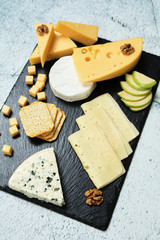 Pieces of cheese on a dark background. Cheeseboard. Sliced ​​apple and nuts on the board. Hard cheese, camembert, roquefort, emmental.