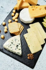 Pieces of cheese on a dark background. Cheeseboard. Sliced ​​apple and nuts on the board. Hard cheese, camembert, roquefort, emmental.