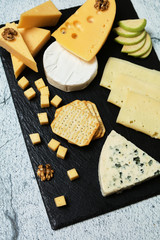 Pieces of cheese on a dark background. Cheeseboard. Sliced ​​apple and nuts on the board. Hard cheese, camembert, roquefort, emmental.