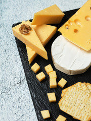 Pieces of cheese on a dark background. Cheeseboard. Sliced ​​apple and nuts on the board. Hard cheese, camembert, roquefort, emmental.