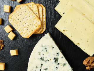 Pieces of cheese on a dark background. Cheeseboard. Sliced ​​apple and nuts on the board. Hard cheese, camembert, roquefort, emmental.