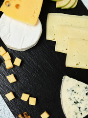 Pieces of cheese on a dark background. Cheeseboard. Sliced ​​apple and nuts on the board. Hard cheese, camembert, roquefort, emmental.