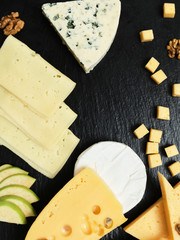 Pieces of cheese on a dark background. Cheeseboard. Sliced ​​apple and nuts on the board. Hard...