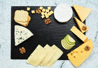 Pieces of cheese on a dark background. Cheeseboard. Sliced ​​apple and nuts on the board. Hard cheese, camembert, roquefort, emmental.