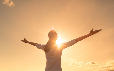 Happy positive woman looking up to the sunset sky with arms up feeling free
