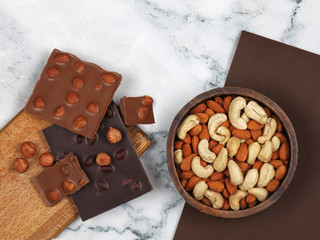 Broken chocolate bars, raw hazelnuts, almonds and cashew on gray marble background