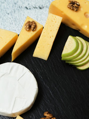 Pieces of cheese on a dark background. Cheeseboard. Sliced ​​apple and nuts on the board. Hard cheese, camembert, roquefort, emmental.