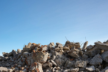 A pile of large gray concrete fragments with protruding fittings against a blue cloudy sky....