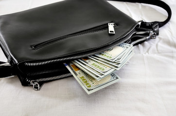 dollars sticking out with a black, women bag on white.