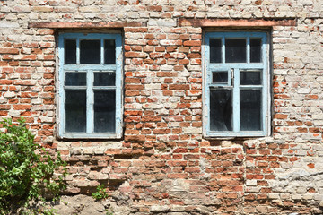 Old small windows of blue color and a brick wall. Exterior of an old house