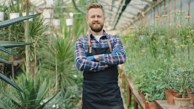 Happy gar portrait in front of the camera he crossed hands and smiling charismatic looking straight to the camera background a very beautiful flower greenhouse
