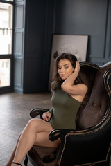 Obraz na płótnie Canvas Beautiful brunette in sexy green bodysuit with naked legs sittin