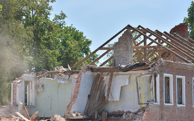 Demolition of an old house with ruined walls and a roof against a blue sky