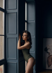 Young sexy girl in green bodysuit poses near the window.
