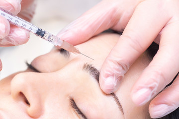 Close-up of a beautician injecting Botox into forehead wrinkles. She holds a syringe. Botox injection. Cosmetics injected womans face