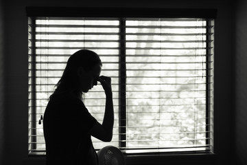 Sad stressed young woman standing next to bedroom window. 