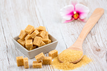 Brown sugar in a square cup and wooden spoon on a wooden table, healthy sugar is used for cooking food or desserts.