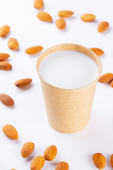 Almond milk with almond on white background. Homemade organic almond milk in a paper cup for healthy breakfast. Vegan milk from almonds nuts in kraft paper cup. Alternative milk. Zero waste