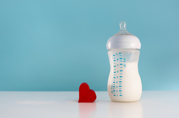 Isolated baby bottle of milk next to heart. Feeding infant concept. 