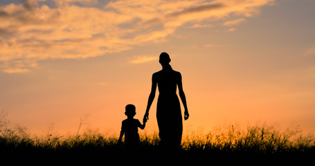 Mother holding Childs hand walking through a field at sunset. 