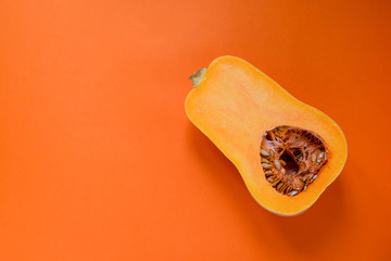Half of the bright ripe pumpkin lies on an orange background. Copy space.