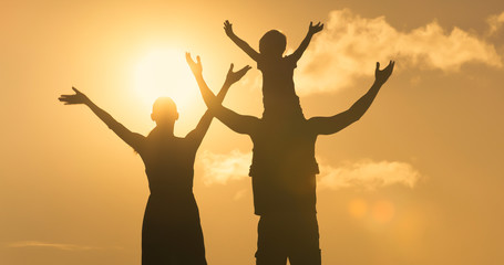 Happy family of three the arms up facing beautiful sunrise. 