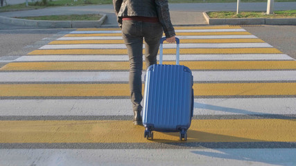 A woman with a blue suitcase walks along a pedestrian crossing.