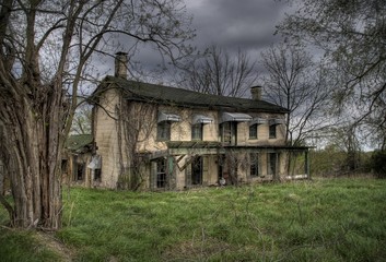 Old abandoned farmhouse in the midwest surrounded by leafless trees and overgrown lawn