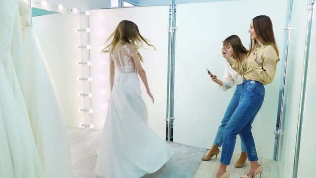 Girls taking photo of happy bride spinning in front of mirror in wedding dress