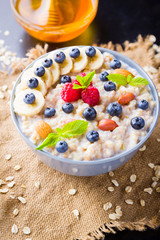 Healthy breakfast. Oatmeal porridge with berries, fruits and honey on dark background. Oatmeal with raspberries, blueberries and almonds on sackcloth